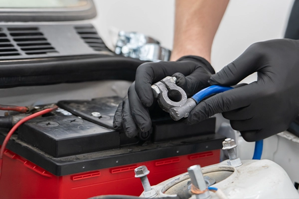 Man with gloves removing negative battery cable from terminal